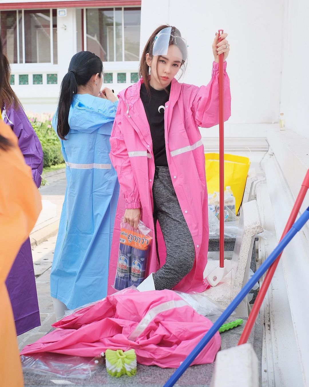 เป้ย ปานวาด ใส่เสื้อกันฝน สีชมพู และ รองเท้าบูท พร้อมน้ำยาล้างห้องน้ำ ไม้ถูพื้น แปรงขัดส้วม