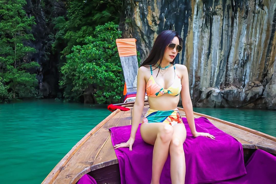 เมย์ พิชญ์นาฏ สาขากร ในชุดว่ายน้ำสีเขียว-เหลือง นั่งอยู่บนเรือหางยาว ที่เกาะห้อง จังหวัดกระบี่
